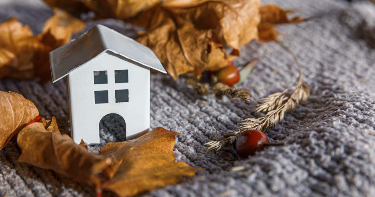 A small toy house on a cozy gray blanket surrounded by autumn leaves, representing home warmth and energy-saving tips for New Jersey homeowners.